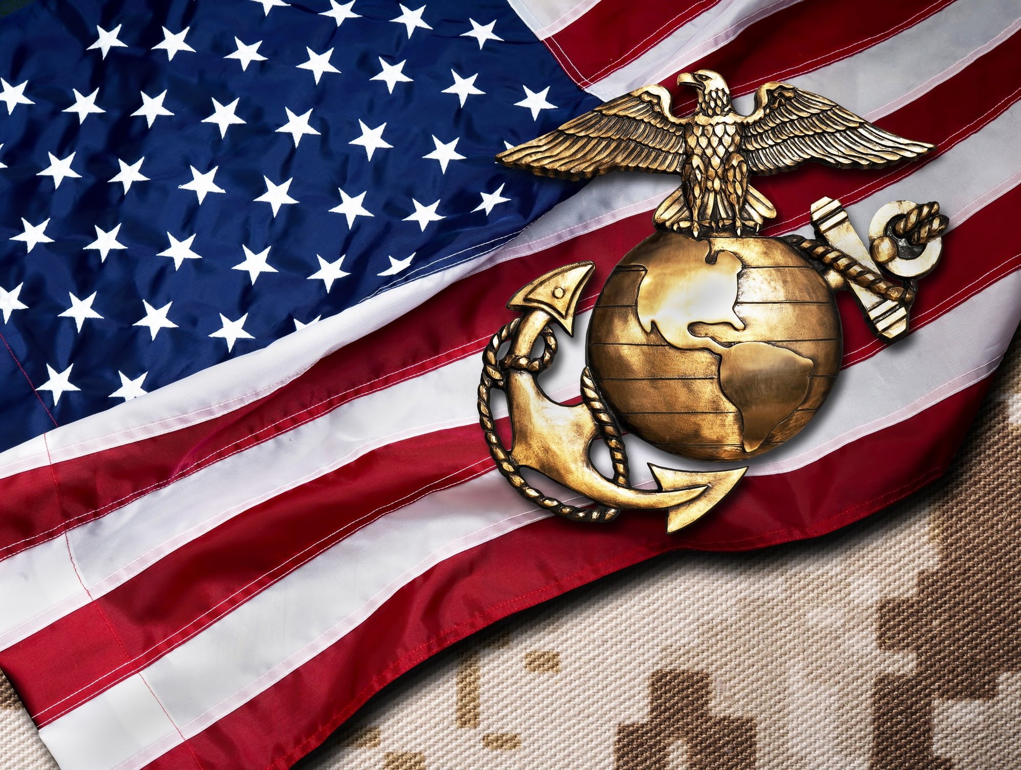 An American flag sits on a camo backdrop while holding up a US Marine Corps emblem.