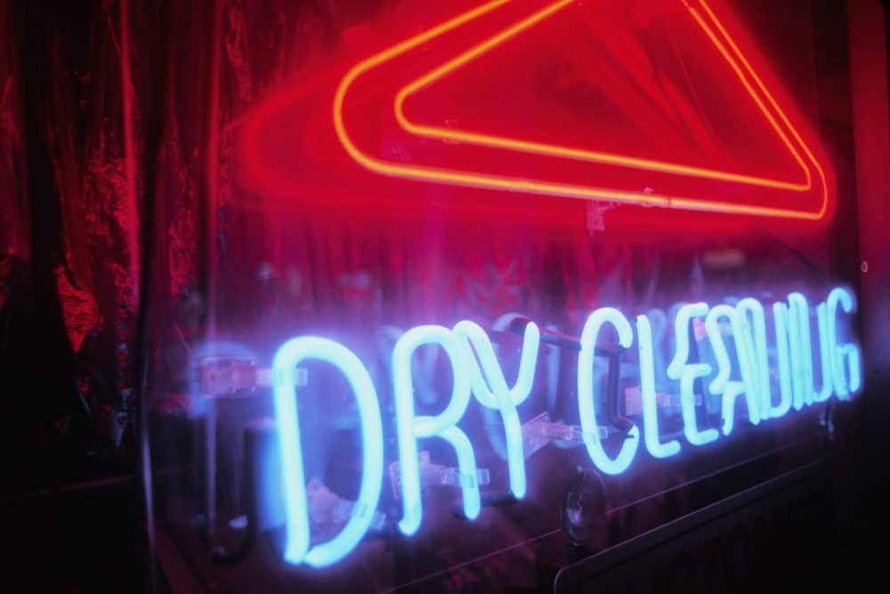 A dry cleaning business’s blue neon sign glows outside at night.